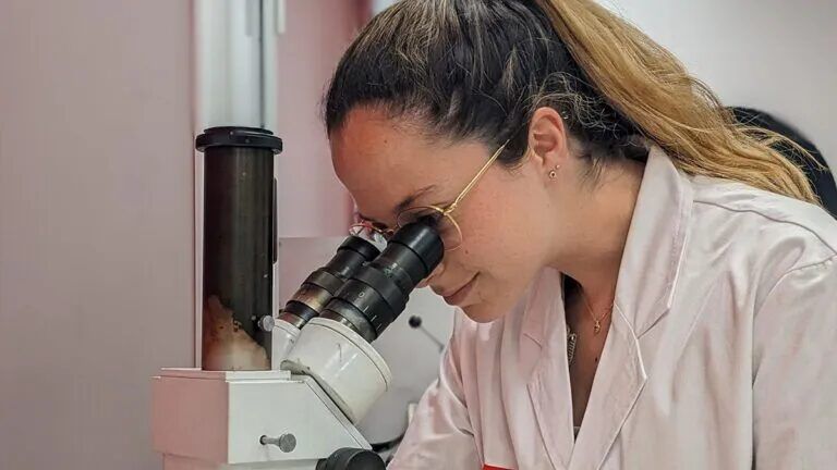 Woman in lab jacket looking through microscope